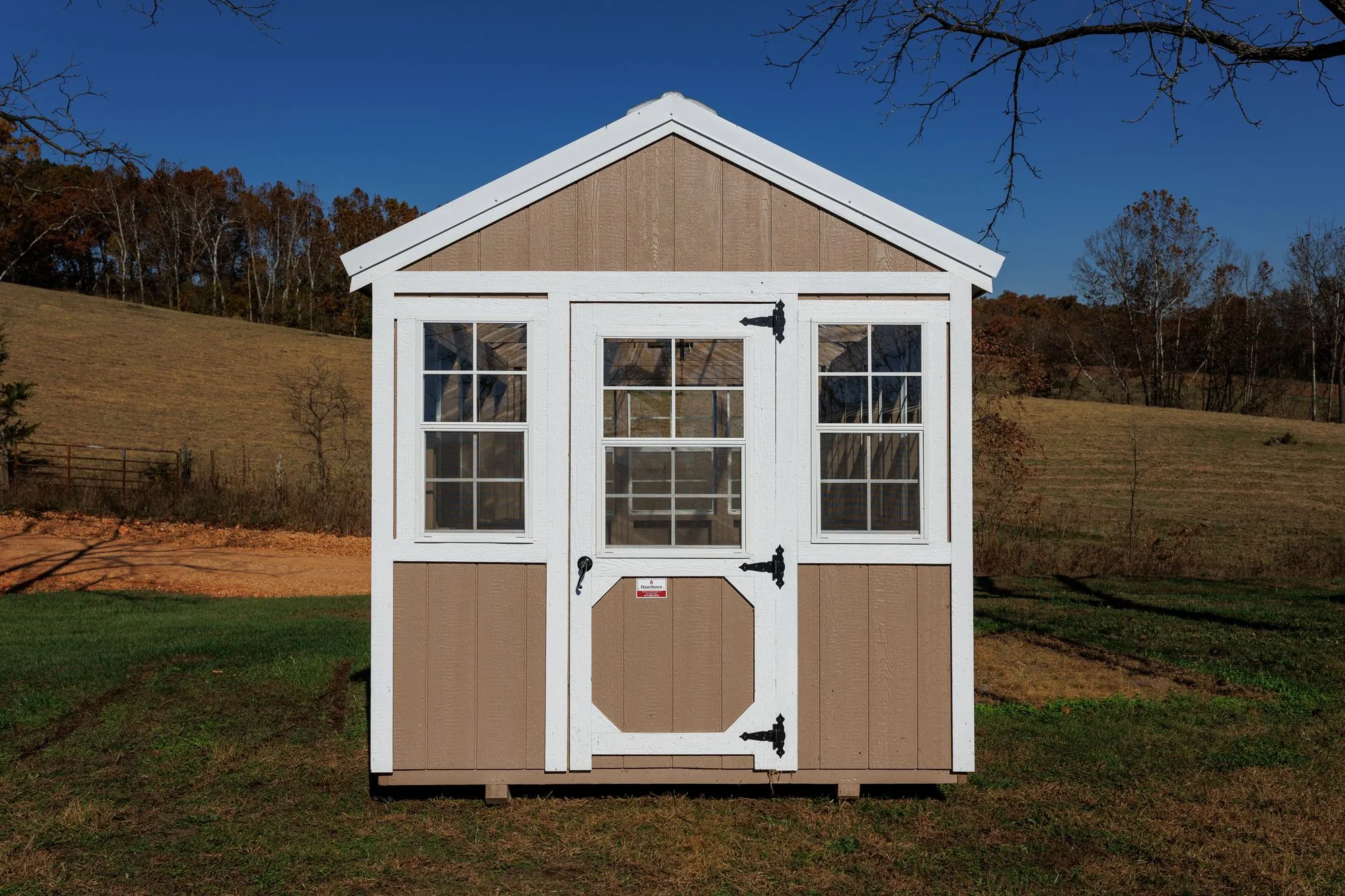 Greenhouse with tan siding with white trim and windows down both sides, on the Hawthorn lot in Rocky Comfort, Missouri