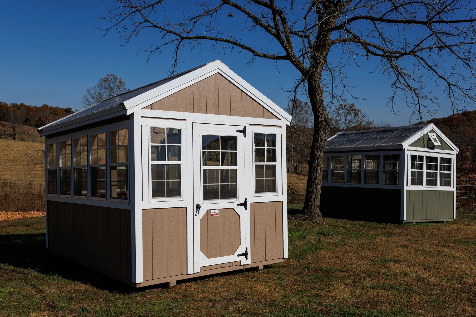 Greenhouse with tan siding with white trim and windows down both sides, on the Hawthorn lot in Rocky Comfort, Missouri
