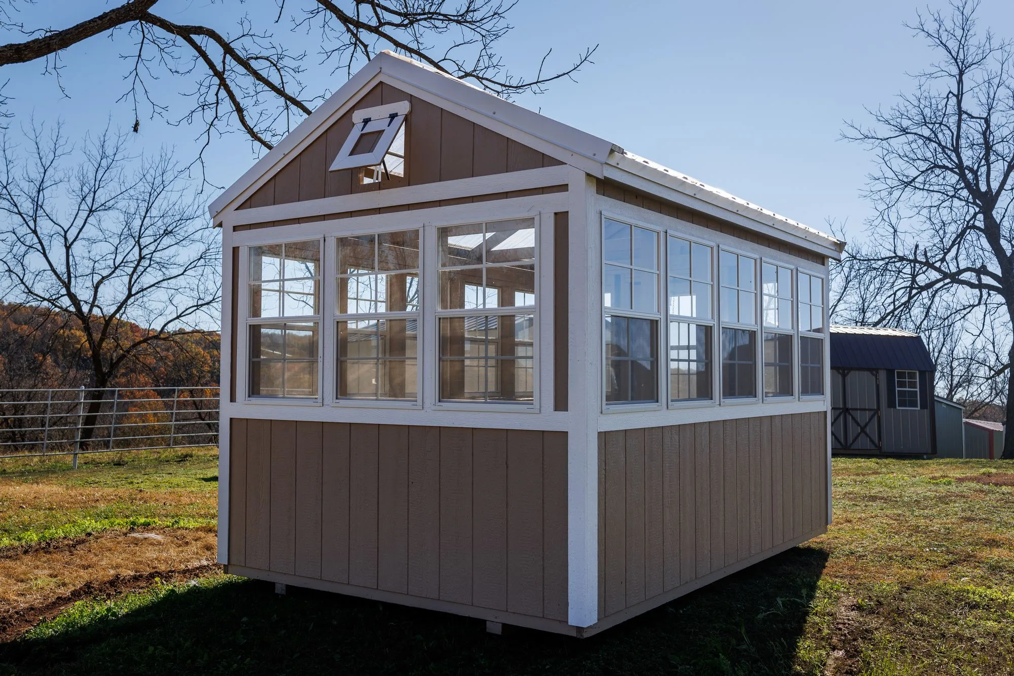 Greenhouse with tan siding with white trim and windows down both sides, on the Hawthorn lot in Rocky Comfort, Missouri