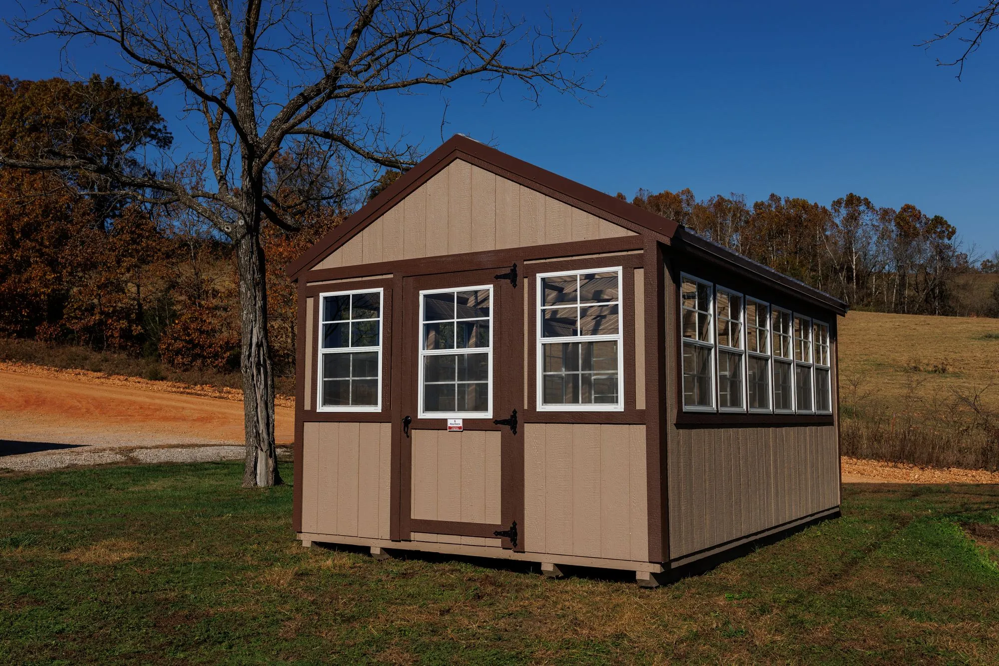 Greenhouse with tan siding with brown trim and a clear corrugated roof, on the Hawthorn lot in Rocky Comfort, Missouri