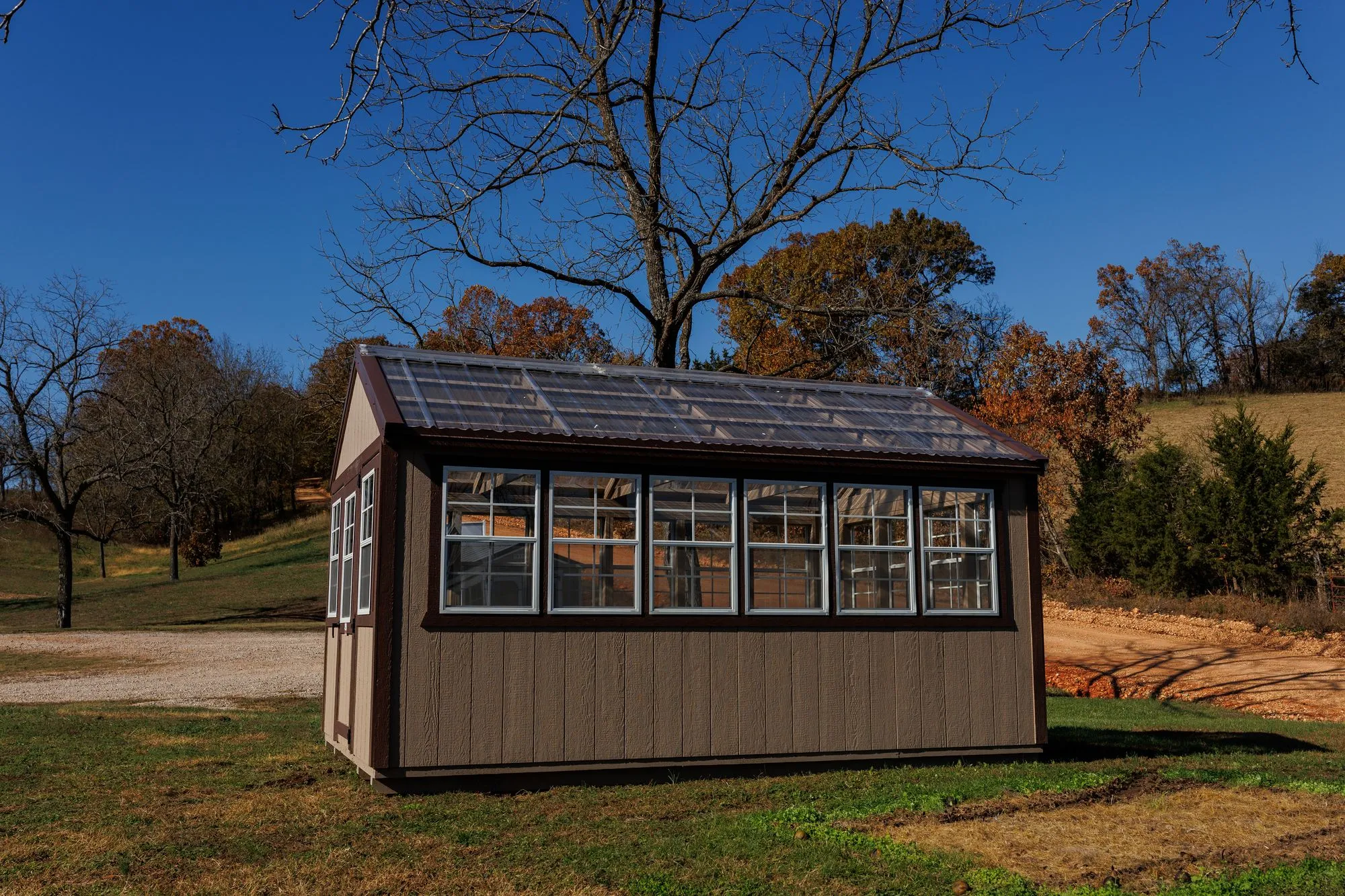Greenhouse with tan siding with brown trim and a clear corrugated roof, on the Hawthorn lot in Rocky Comfort, Missouri