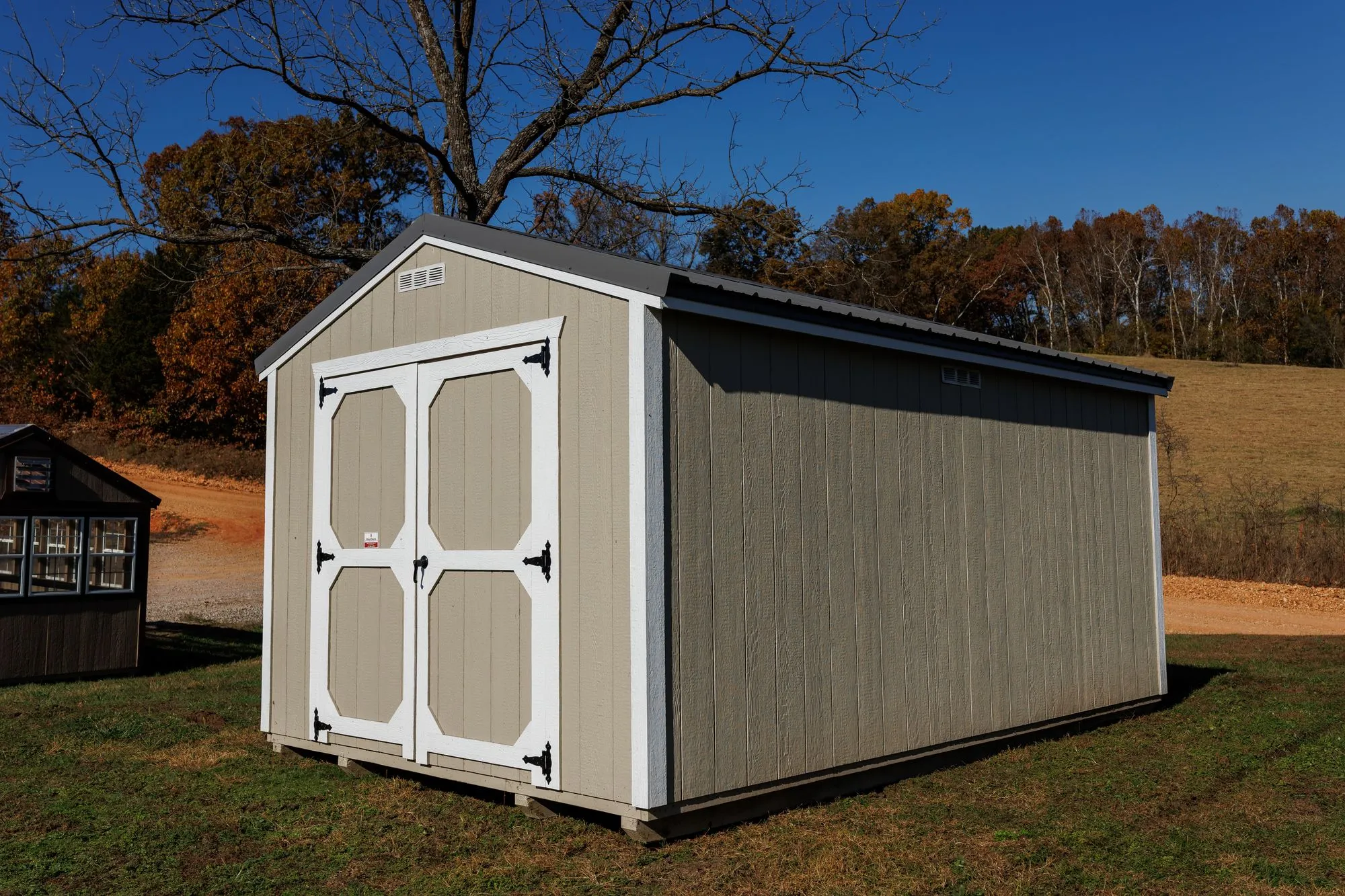 Utility Shed with taupe siding, white trim, charcoal roof, white octagon-panel doors, on the Hawthorn lot in Rocky Comfort, Missouri