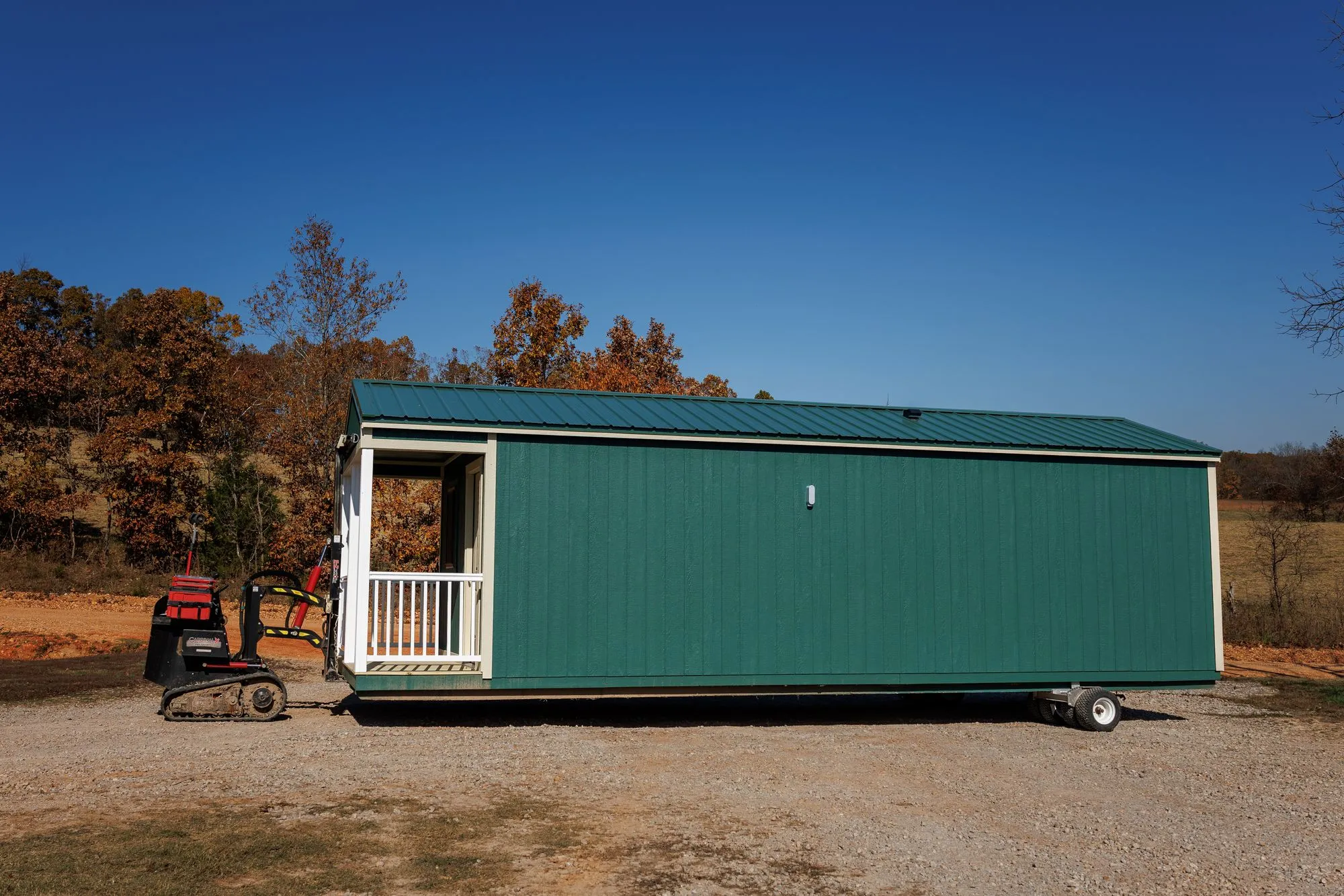 A tracked building mover positioning a long green Hawthorn cabin on a gravel pad