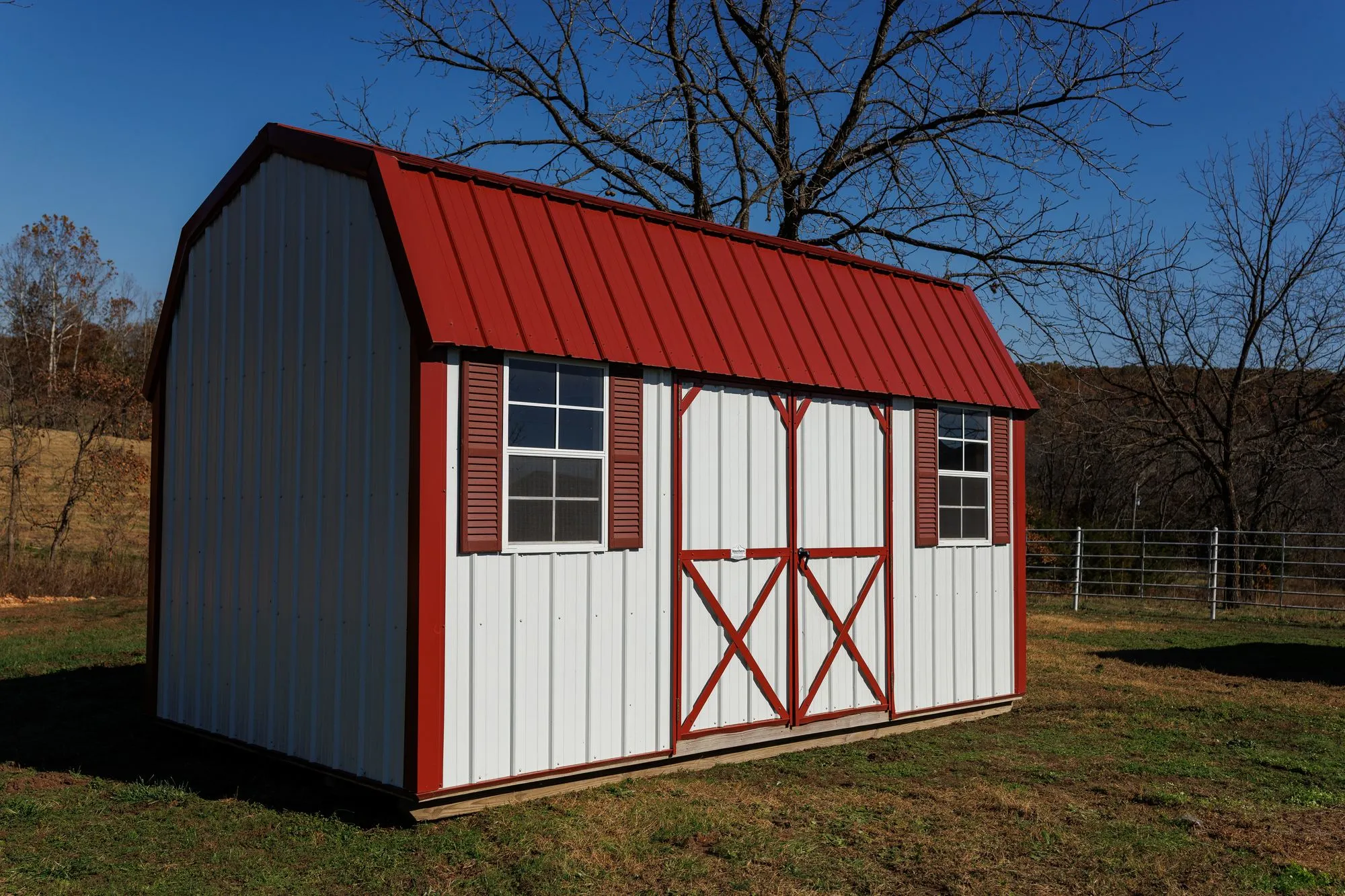 Lofted Garden Barn with white metal siding, red trim and roof, on the Hawthorn lot in Rocky Comfort, Missouri