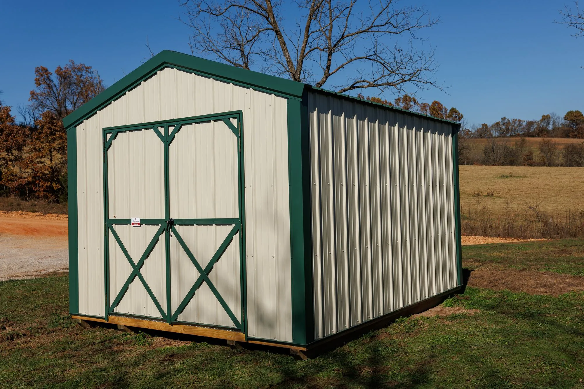 Utility Shed with ivory metal siding with green trim and roof, green X-braced doors, on the Hawthorn lot in Rocky Comfort, Missouri