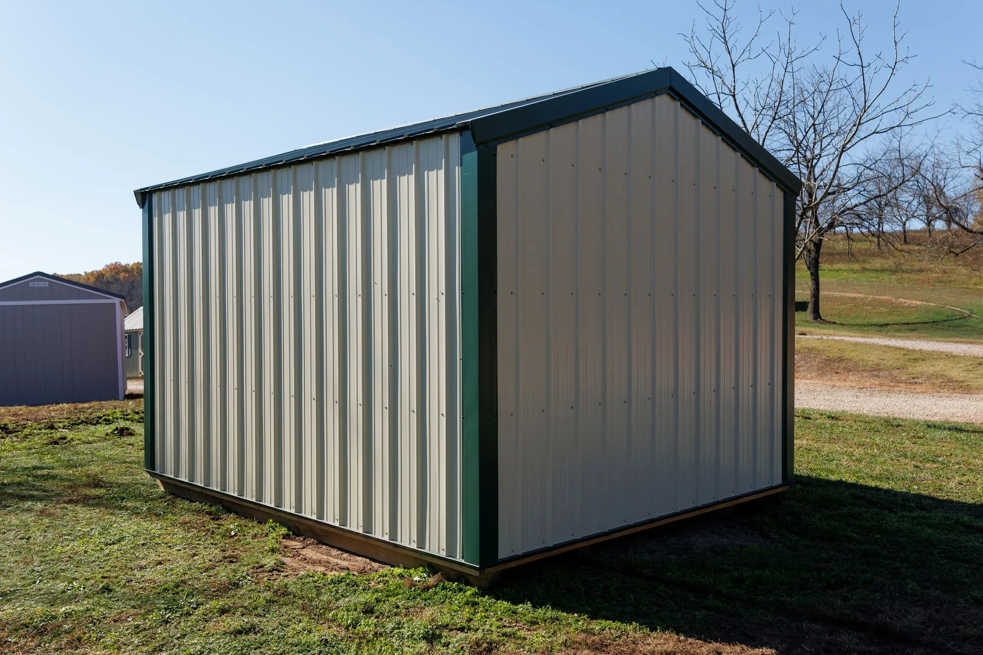 Utility Shed with ivory metal siding with green trim and roof, green X-braced doors, on the Hawthorn lot in Rocky Comfort, Missouri