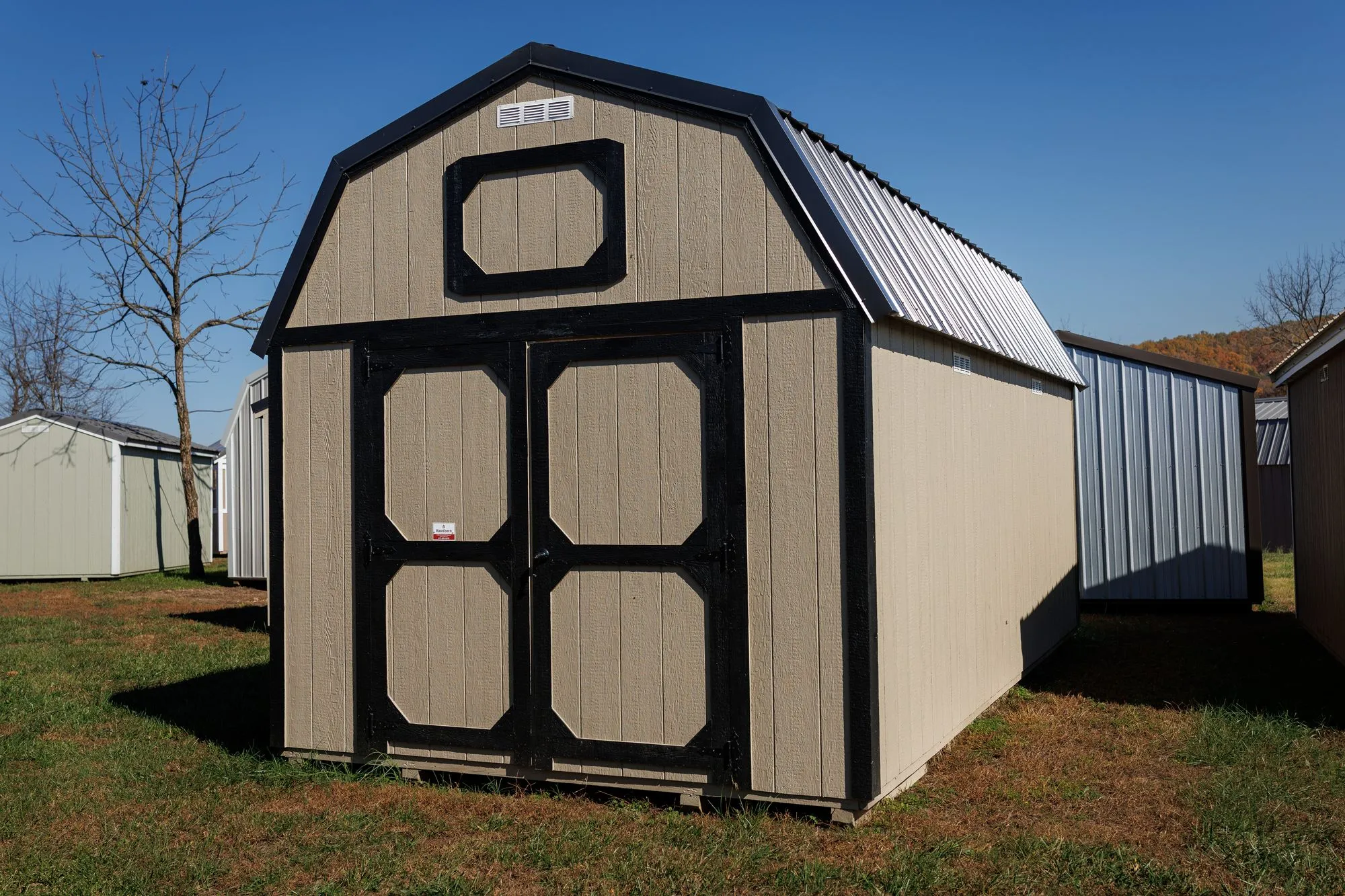 Lofted Barn with tan siding with black trim and roof, octagon-panel doors, on the Hawthorn lot in Rocky Comfort, Missouri