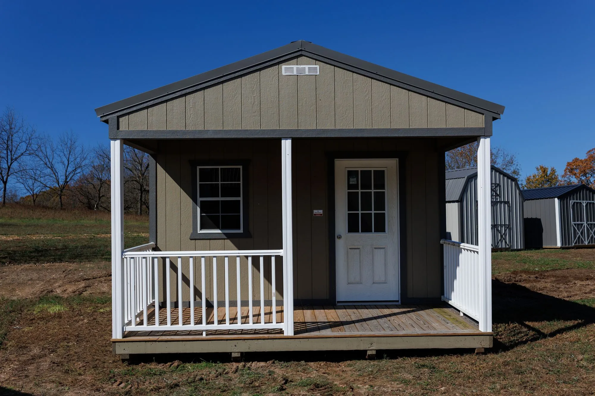 Cabin with olive-taupe siding, charcoal trim and roof, front porch with white railings, on the Hawthorn lot in Rocky Comfort, Missouri