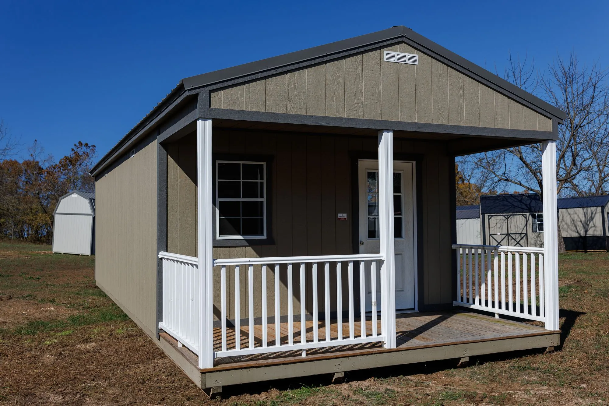 Cabin with olive-taupe siding, charcoal trim and roof, front porch with white railings, on the Hawthorn lot in Rocky Comfort, Missouri