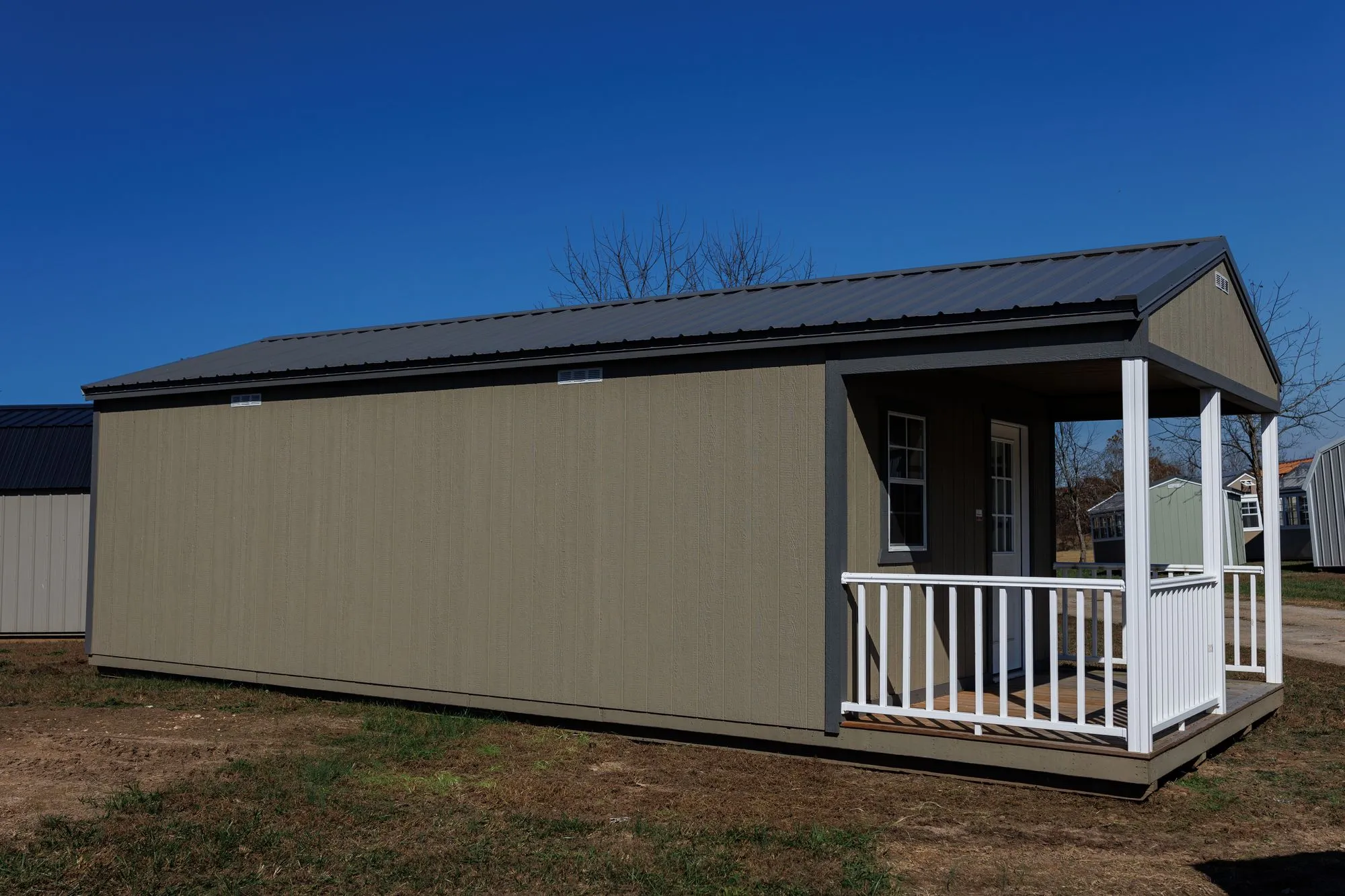 Cabin with olive-taupe siding, charcoal trim and roof, front porch with white railings, on the Hawthorn lot in Rocky Comfort, Missouri