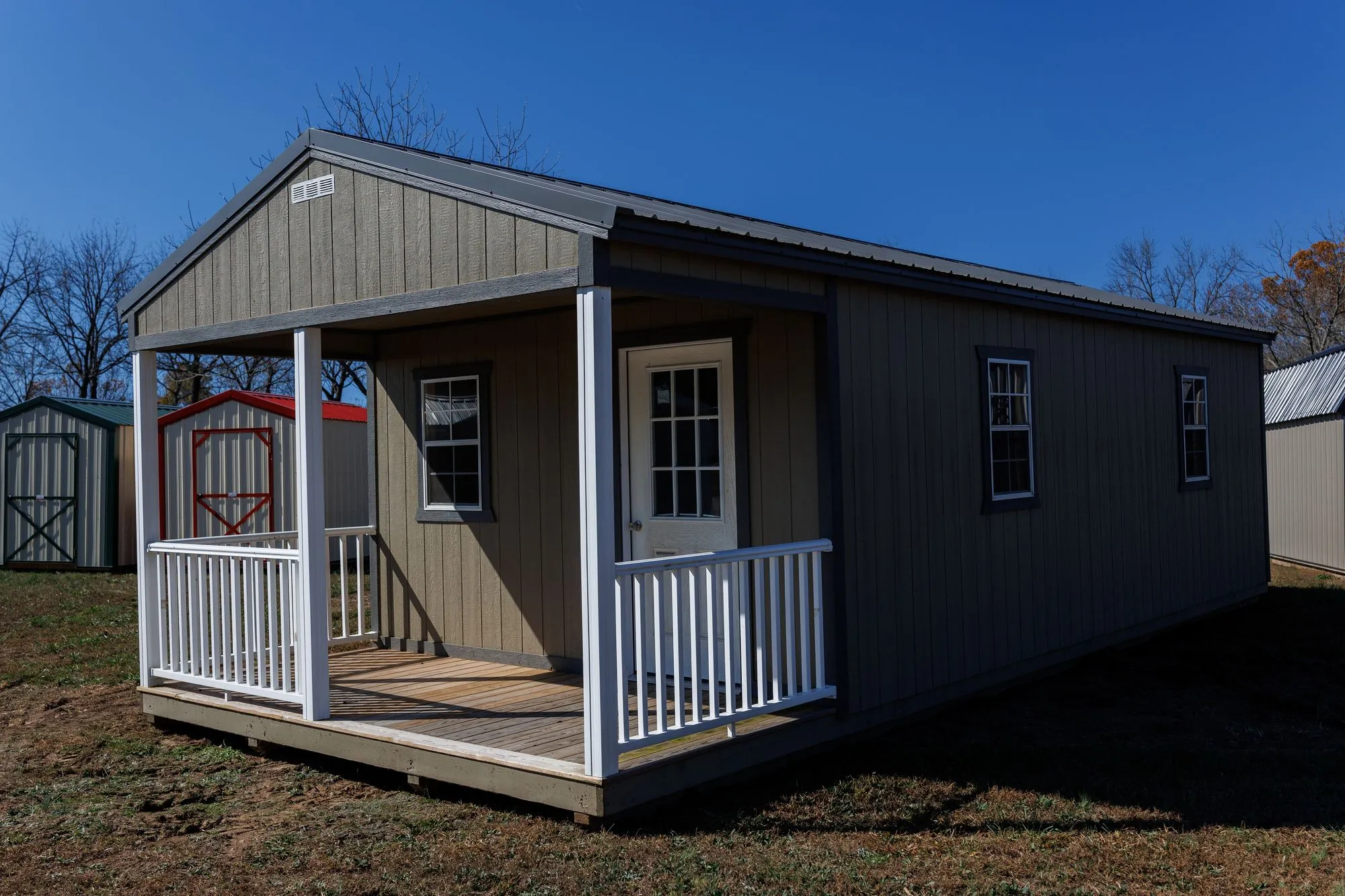 Cabin with olive-taupe siding, charcoal trim and roof, front porch with white railings, on the Hawthorn lot in Rocky Comfort, Missouri