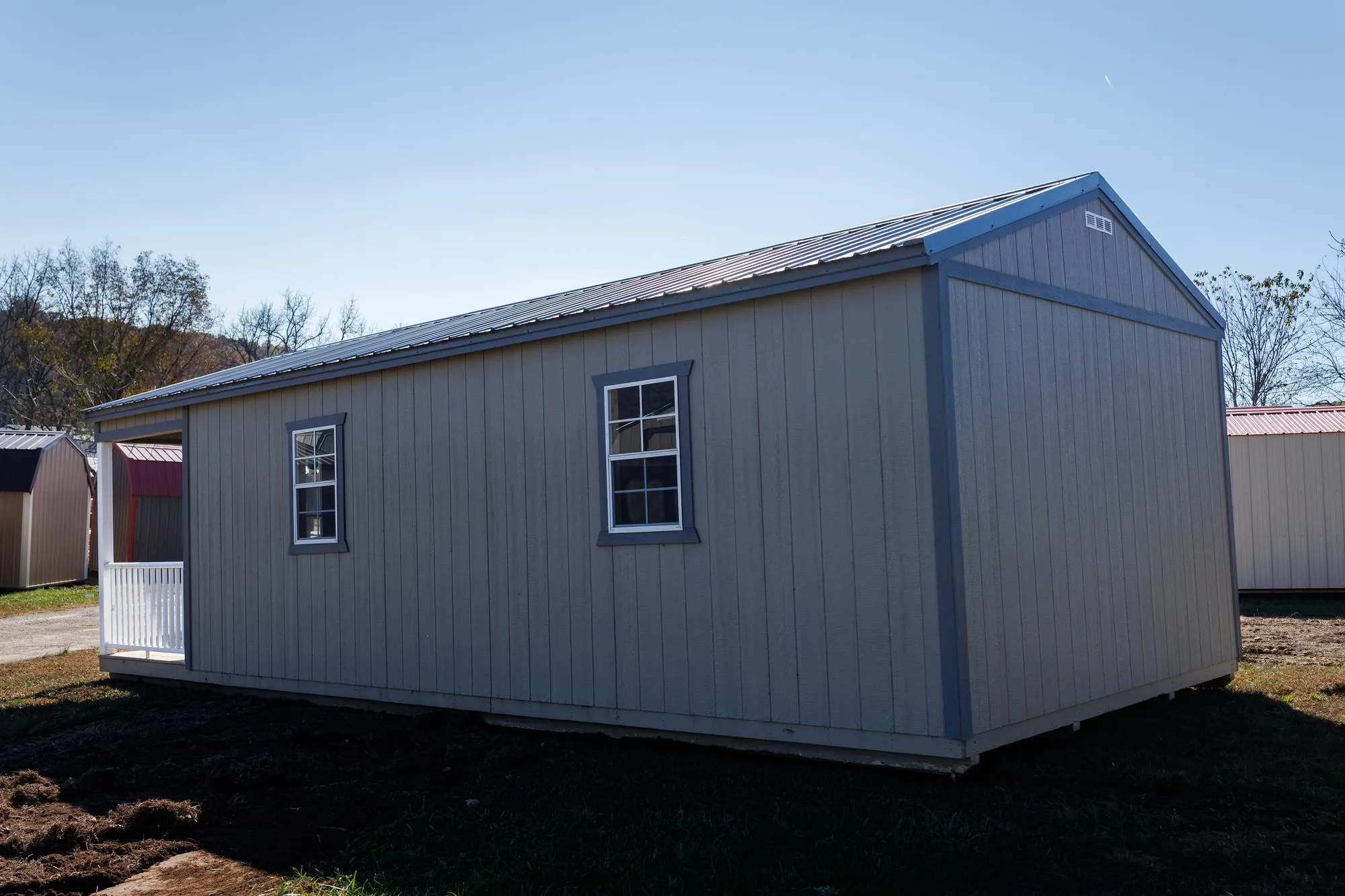 Cabin with olive-taupe siding, charcoal trim and roof, front porch with white railings, on the Hawthorn lot in Rocky Comfort, Missouri