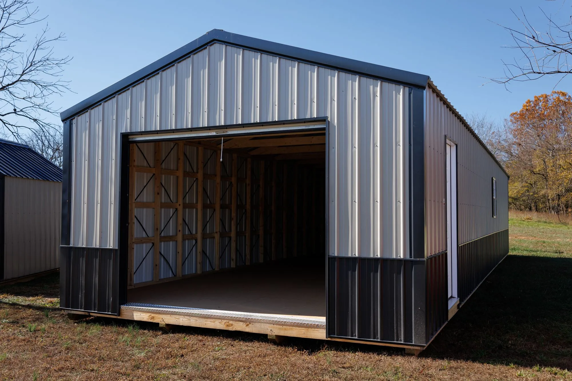 Portable Garage with silver metal siding with a black base, black trim and roof, on the Hawthorn lot in Rocky Comfort, Missouri