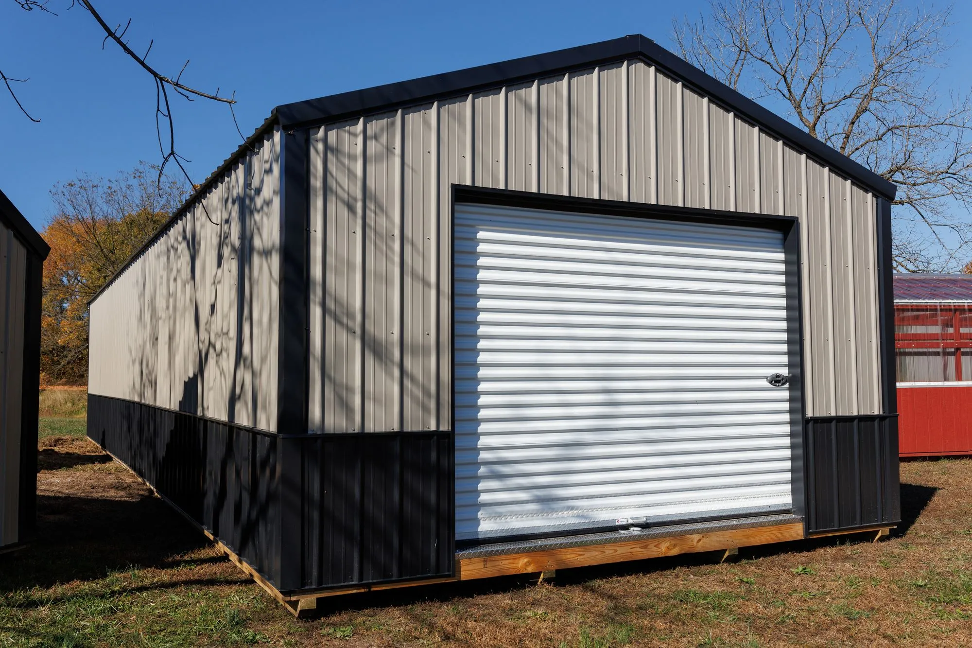 Portable Garage with silver metal siding with a black base, black trim and roof, on the Hawthorn lot in Rocky Comfort, Missouri
