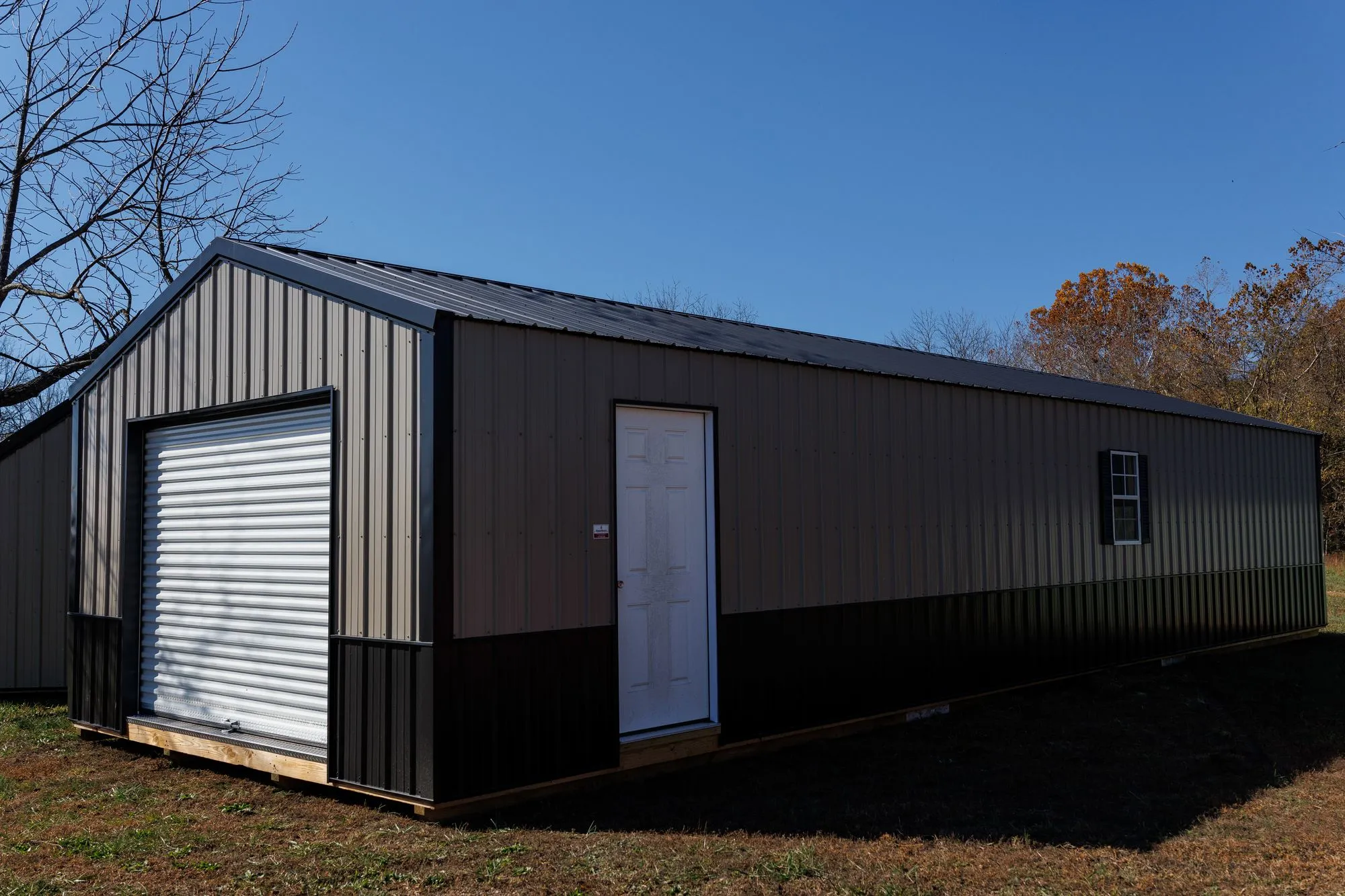 Portable Garage with silver metal siding with a black base, black trim and roof, on the Hawthorn lot in Rocky Comfort, Missouri