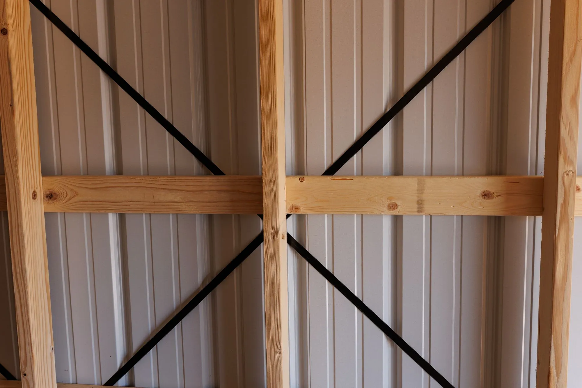Wood wall framing with black diagonal bracing behind white metal siding inside a Hawthorn building