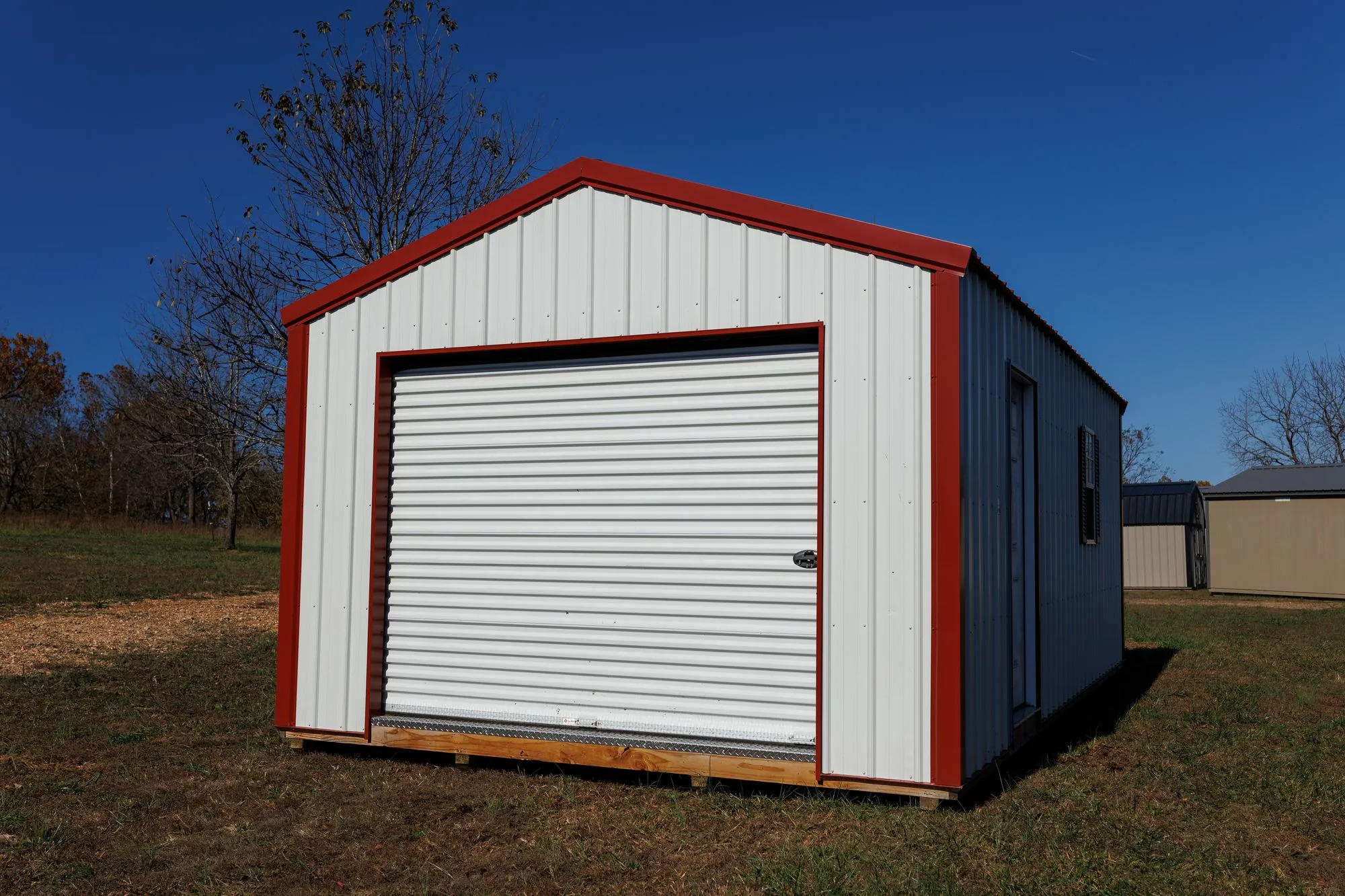 Portable Garage with white metal siding with red trim, on the Hawthorn lot in Rocky Comfort, Missouri