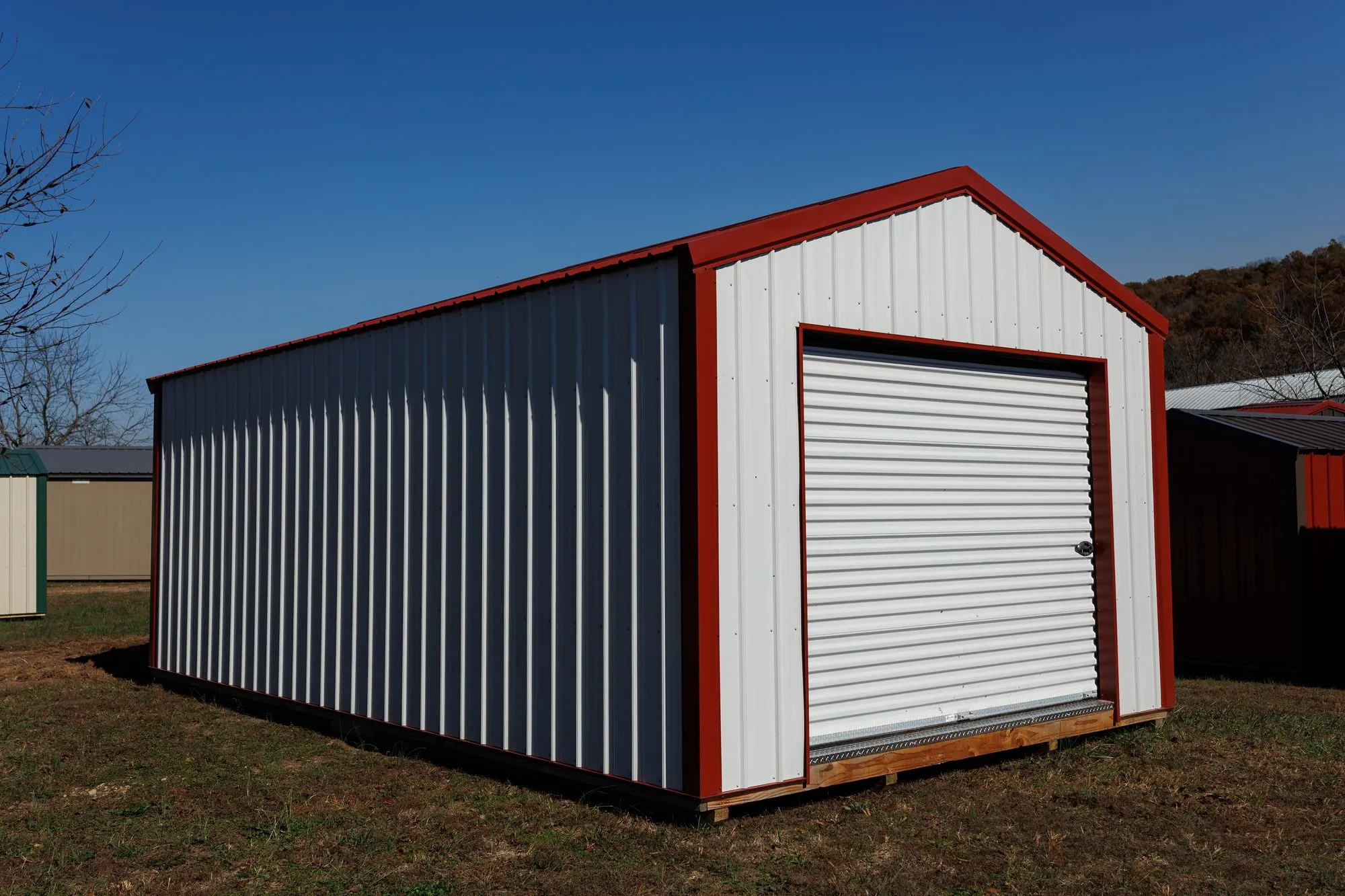 Portable Garage with white metal siding with red trim, on the Hawthorn lot in Rocky Comfort, Missouri