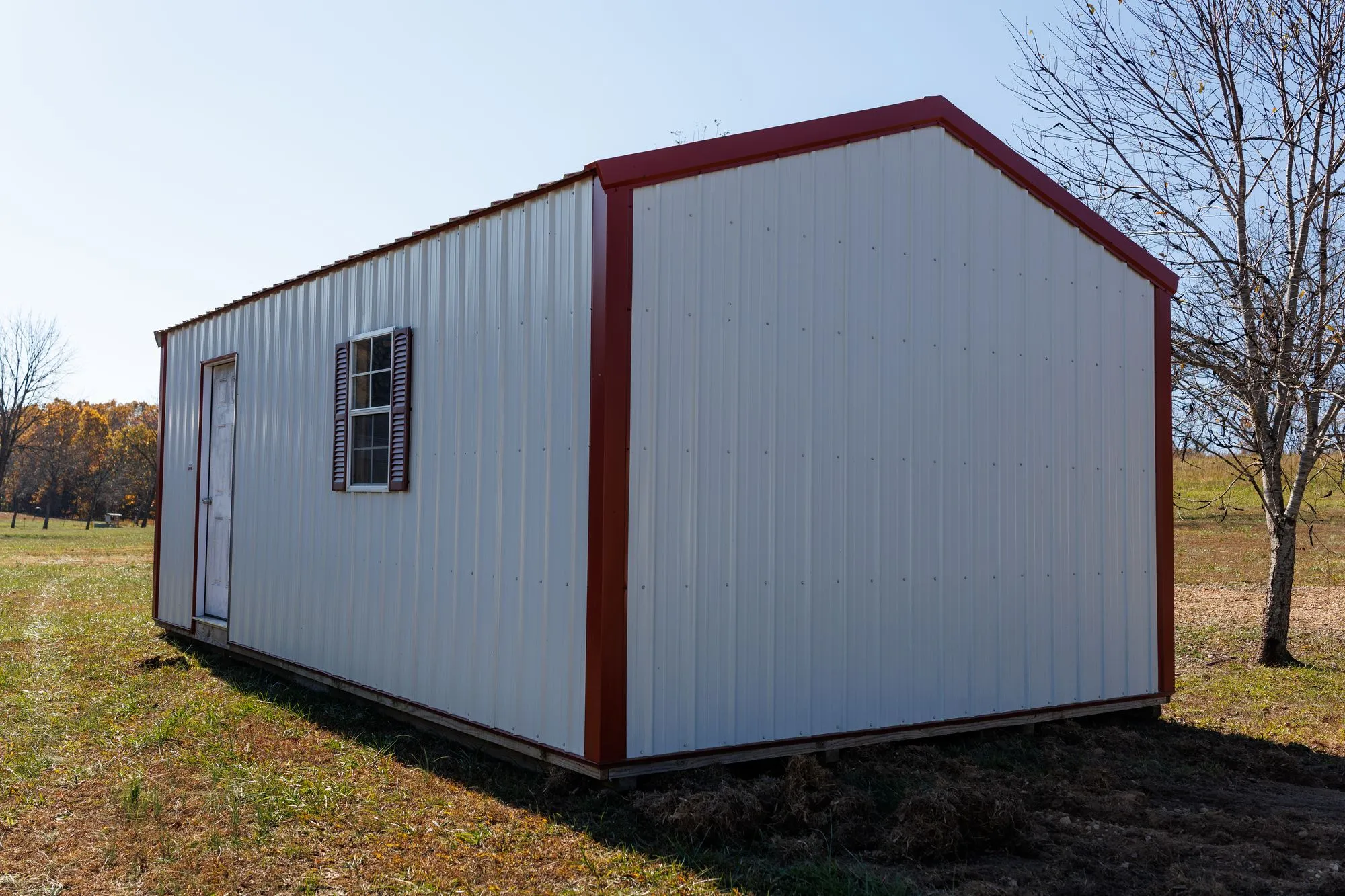 Portable Garage with white metal siding with red trim, on the Hawthorn lot in Rocky Comfort, Missouri