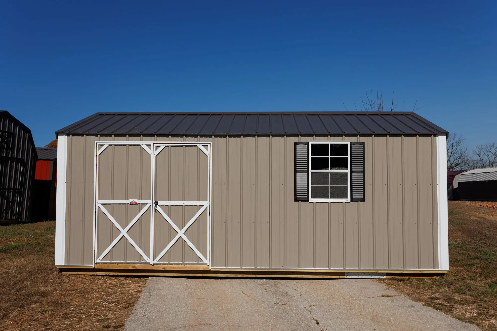 Garden Shed with clay metal siding, white trim, black roof, white X-braced doors, on the Hawthorn lot in Rocky Comfort, Missouri