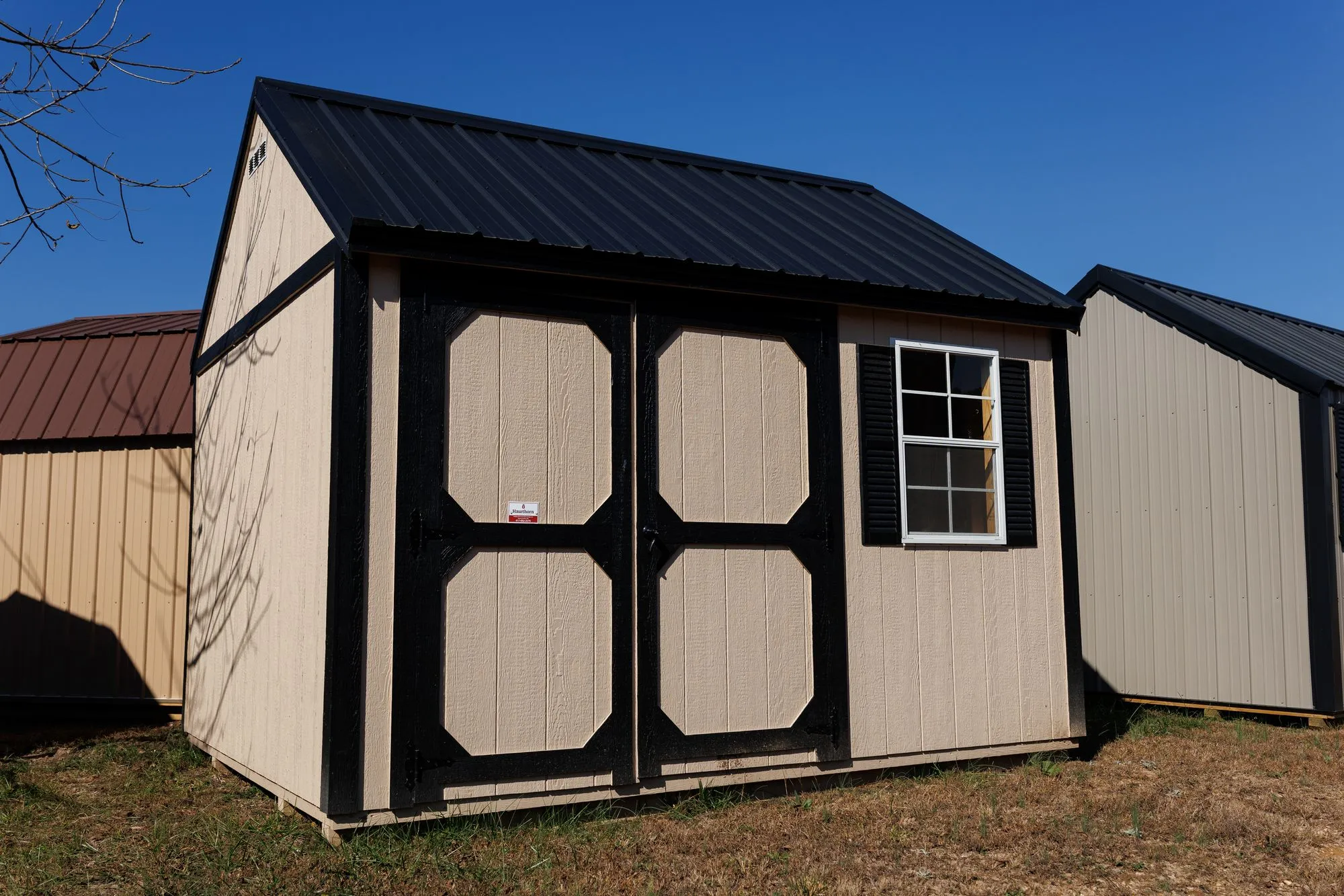 Garden Shed with tan siding, black trim and roof, black-framed octagon-panel doors, on the Hawthorn lot in Rocky Comfort, Missouri