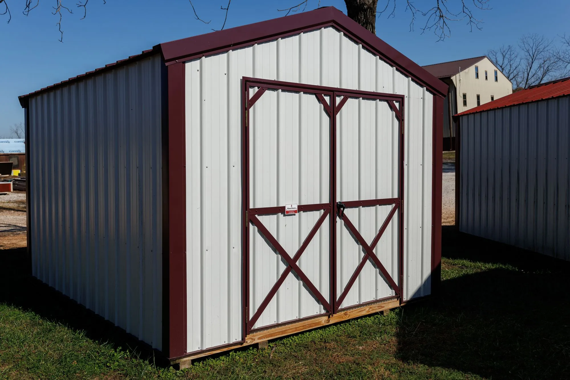 Utility Shed with white metal siding, burgundy trim and roof, on the Hawthorn lot in Rocky Comfort, Missouri