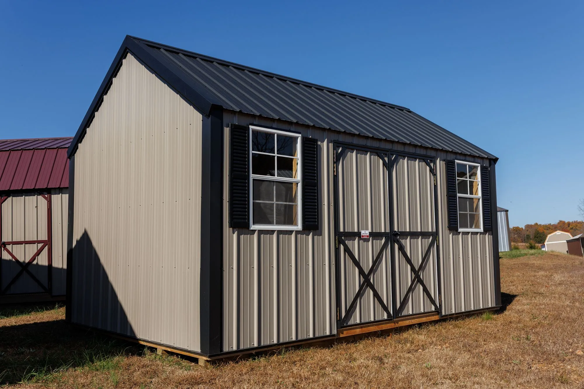 Lofted Garden Shed with clay metal siding, black trim and roof, black X-braced doors, two windows, on the Hawthorn lot in Rocky Comfort, Missouri