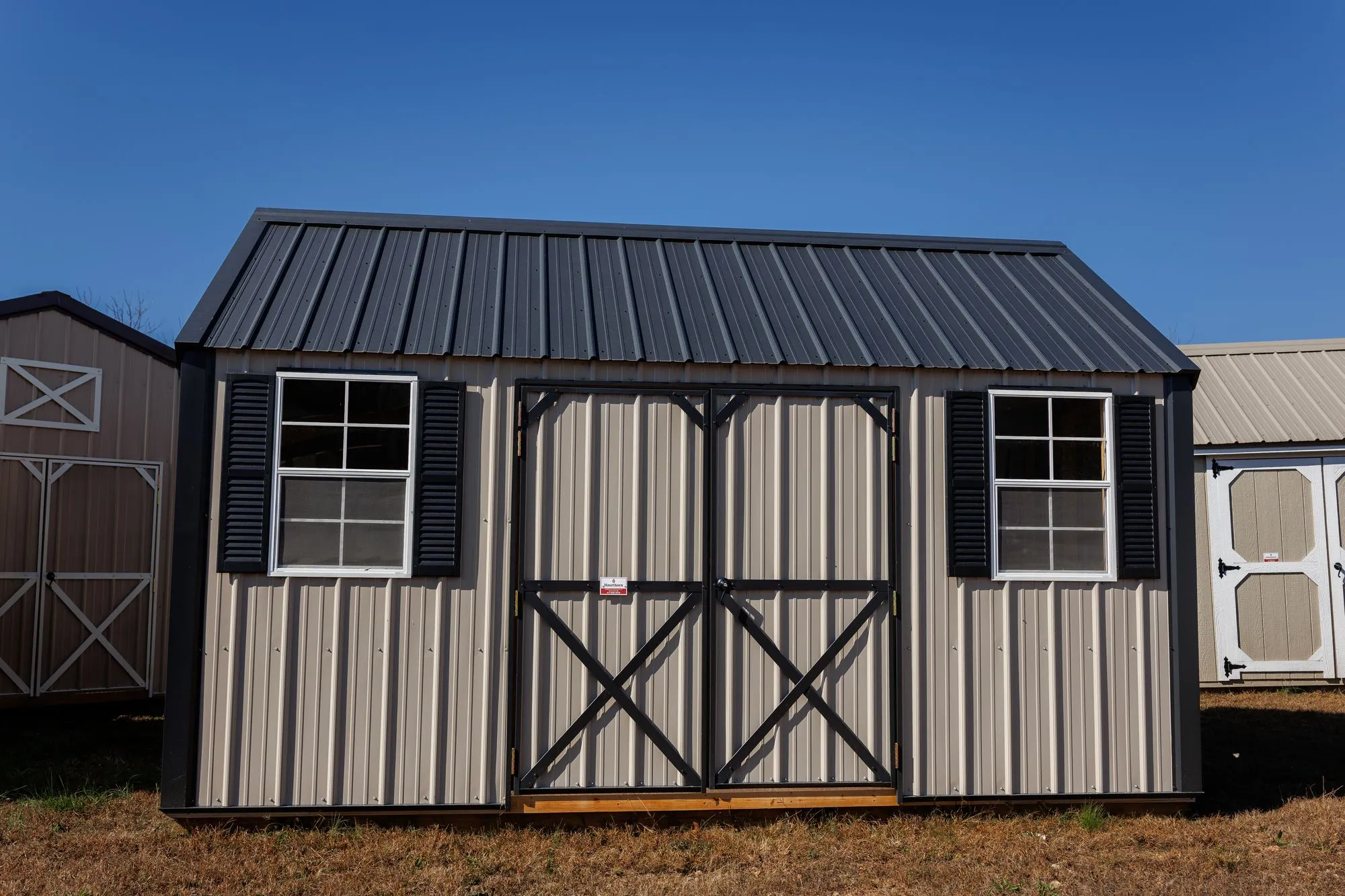 Lofted Garden Shed with clay metal siding, black trim and roof, black X-braced doors, two windows, on the Hawthorn lot in Rocky Comfort, Missouri
