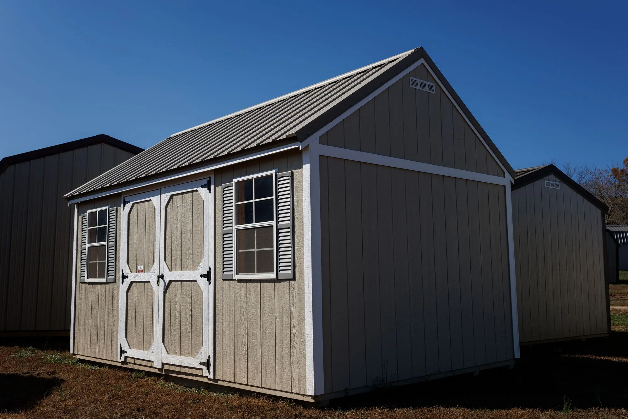 Lofted Garden Shed with tan siding, white trim, clay roof, white octagon-panel doors, two windows, on the Hawthorn lot in Rocky Comfort, Missouri