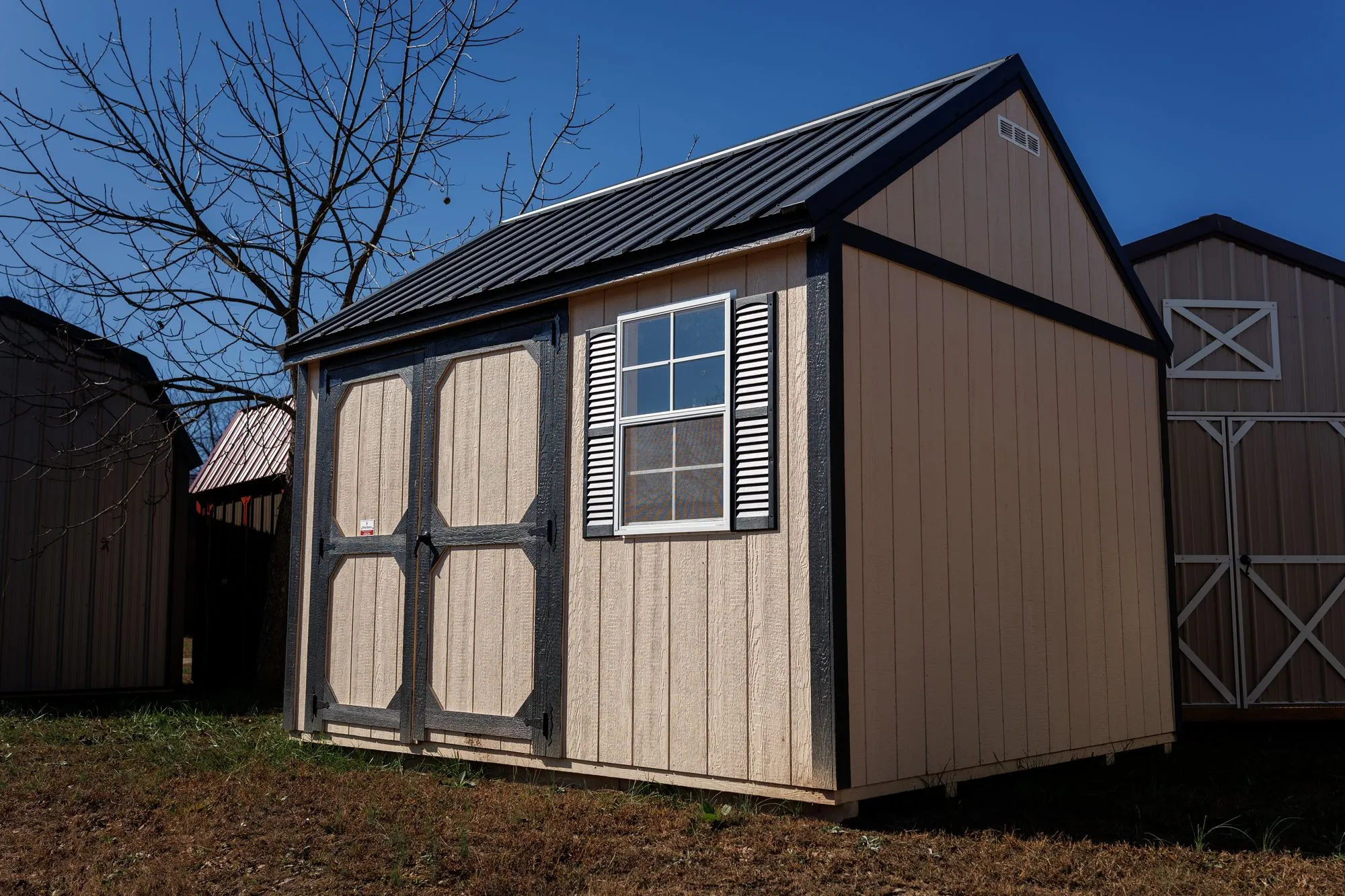 Garden Shed with tan siding, black trim and roof, black-framed octagon-panel doors, on the Hawthorn lot in Rocky Comfort, Missouri