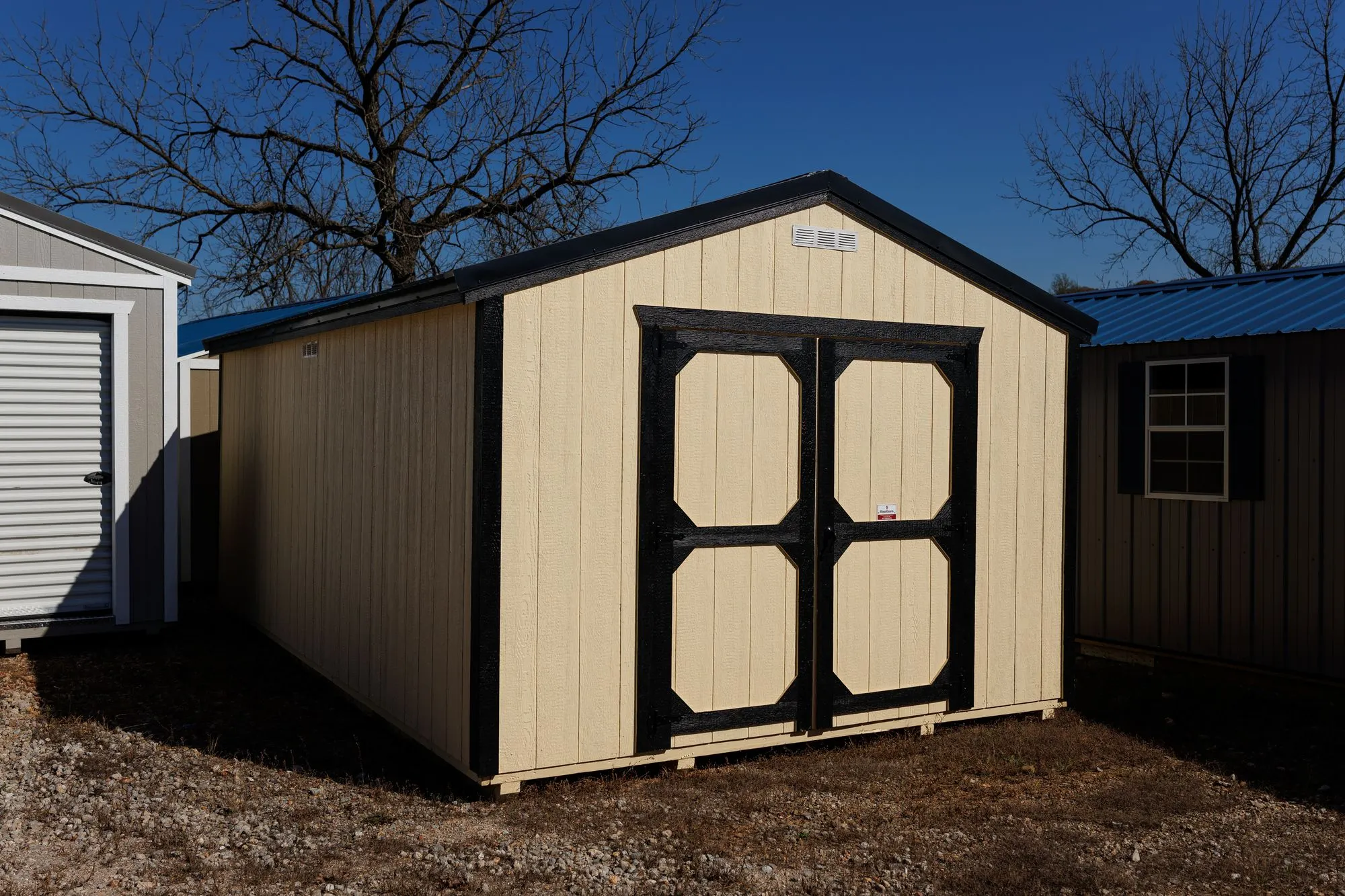 Utility Shed with cream siding, black trim and roof, black-framed octagon-panel doors, on the Hawthorn lot in Rocky Comfort, Missouri