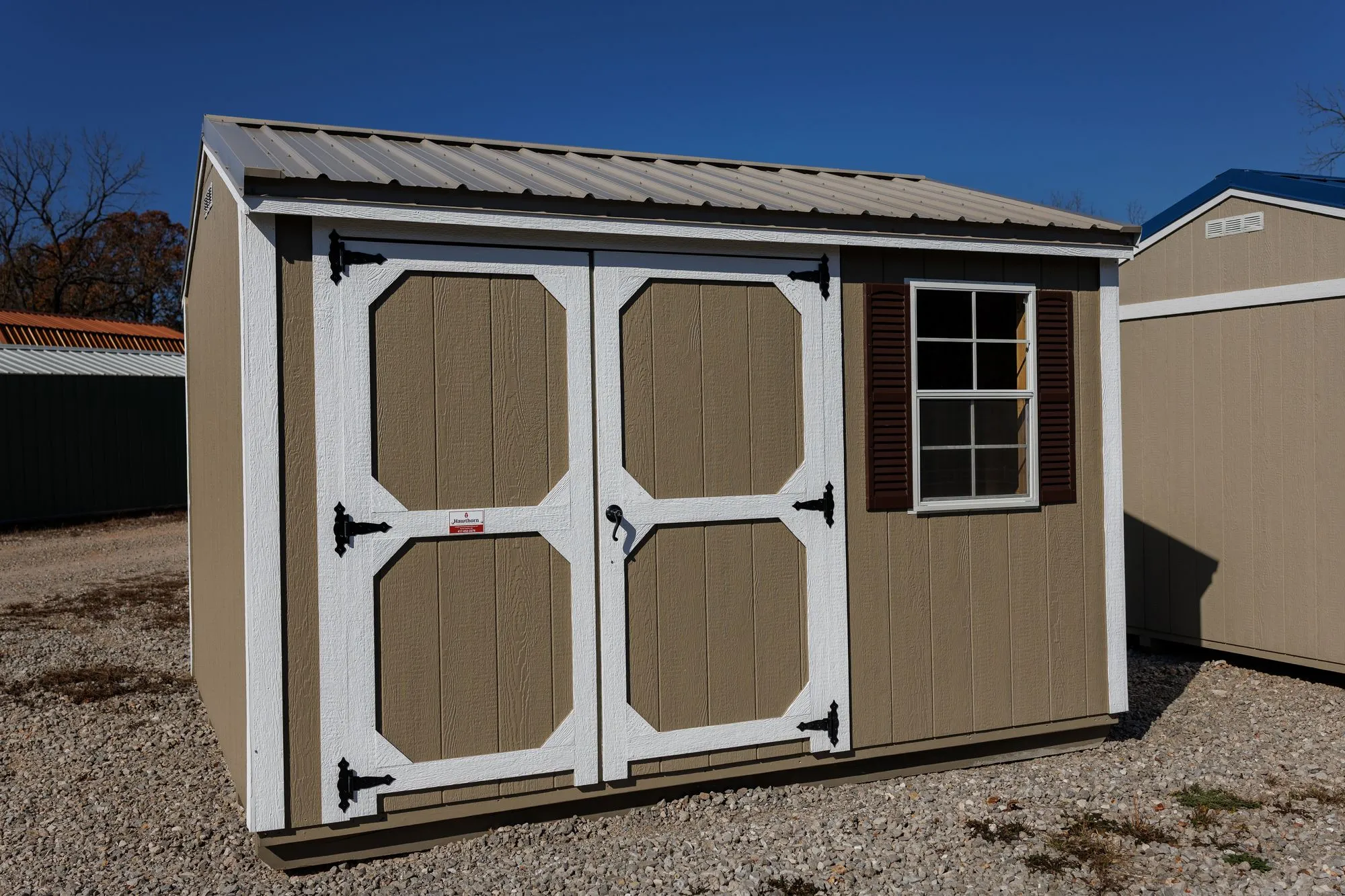 Garden Shed with clay siding, white trim, galvalume roof, white-framed doors, on the Hawthorn lot in Rocky Comfort, Missouri