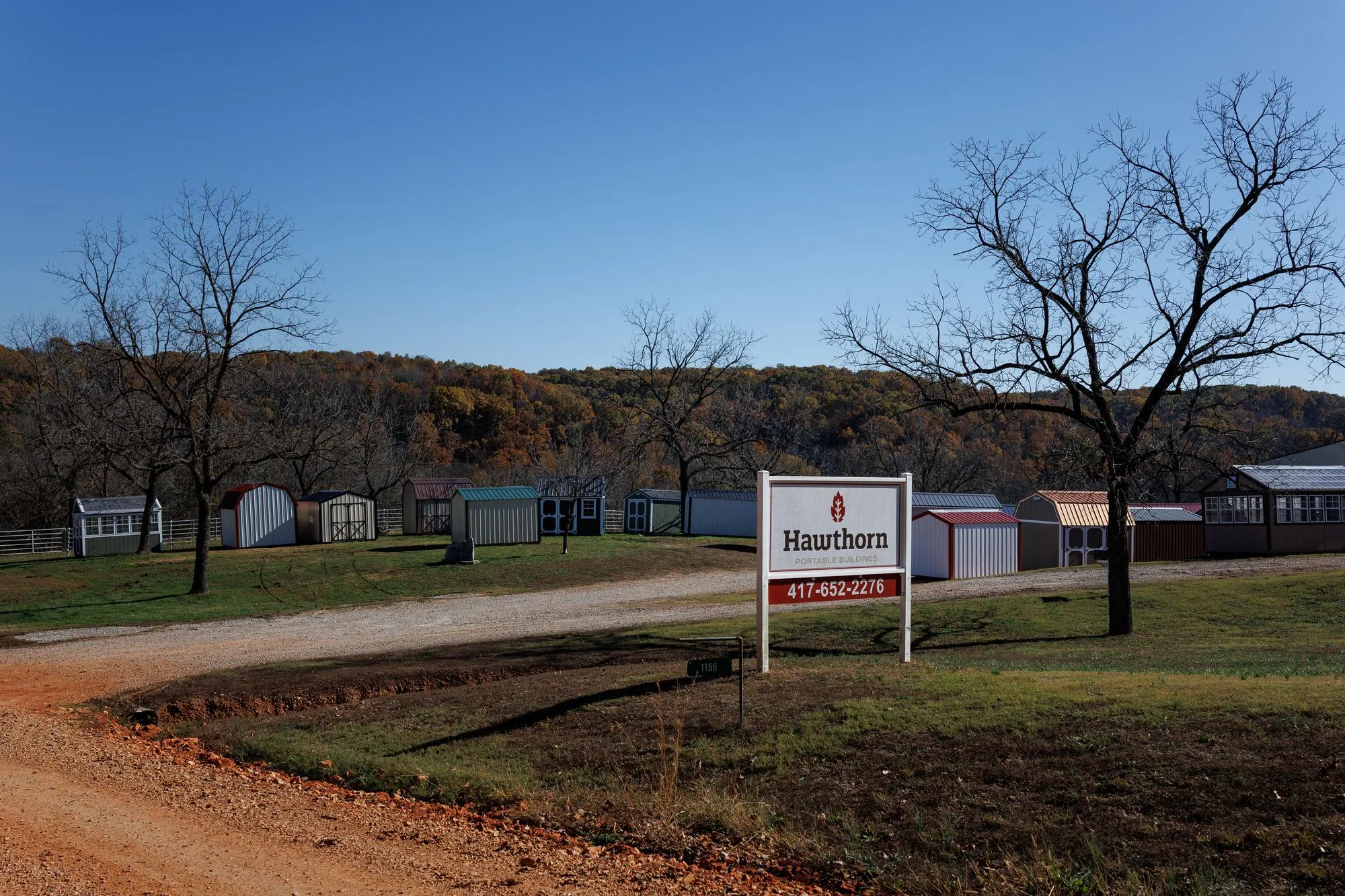 The Hawthorn Portable Buildings sign beside the gravel drive at the lot in Rocky Comfort, Missouri, with buildings behind it