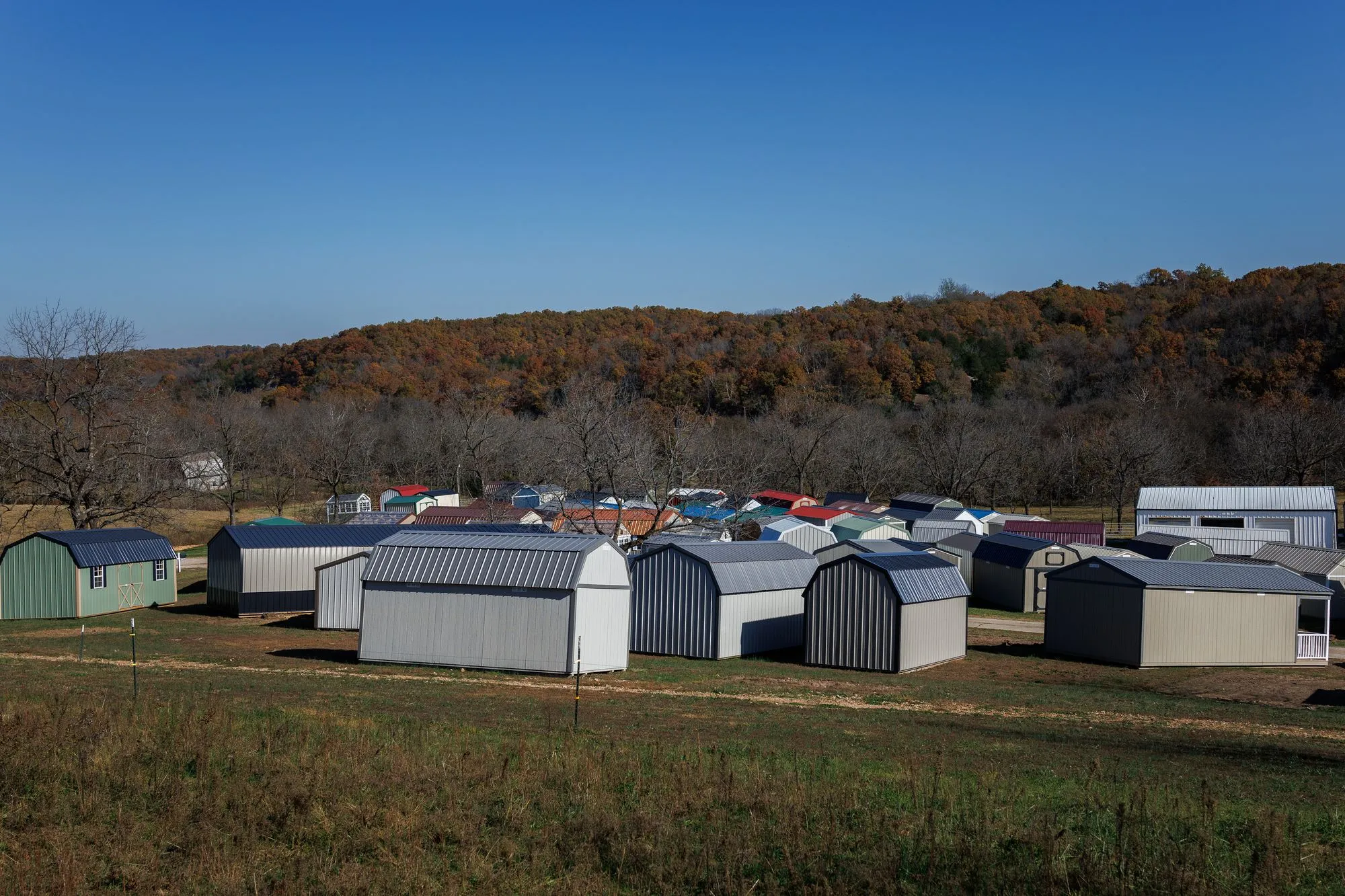 Rows of Hawthorn sheds and barns on the lot in Rocky Comfort, Missouri, with wooded hills behind
